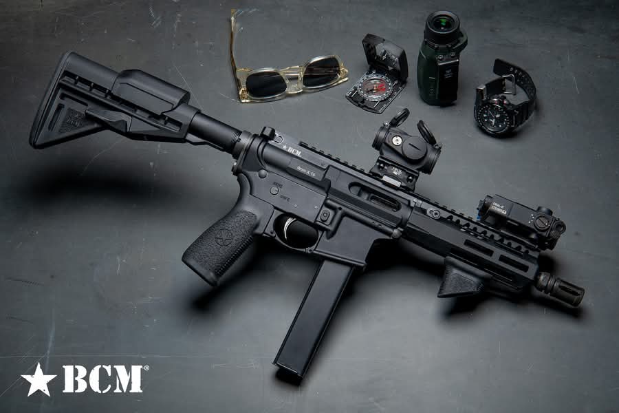 The BCM9, a black AR-pattern 9mm carbine with a collapsible stock, red dot optic, and weapon light, shown in a BCM teaser image